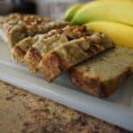 Keto banana bread slices on cutting board next to whole bananas.
