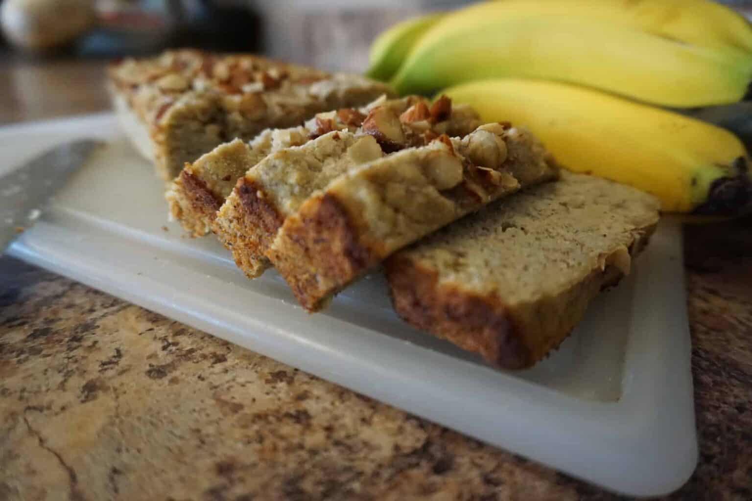 Keto banana bread slices on cutting board next to whole bananas.