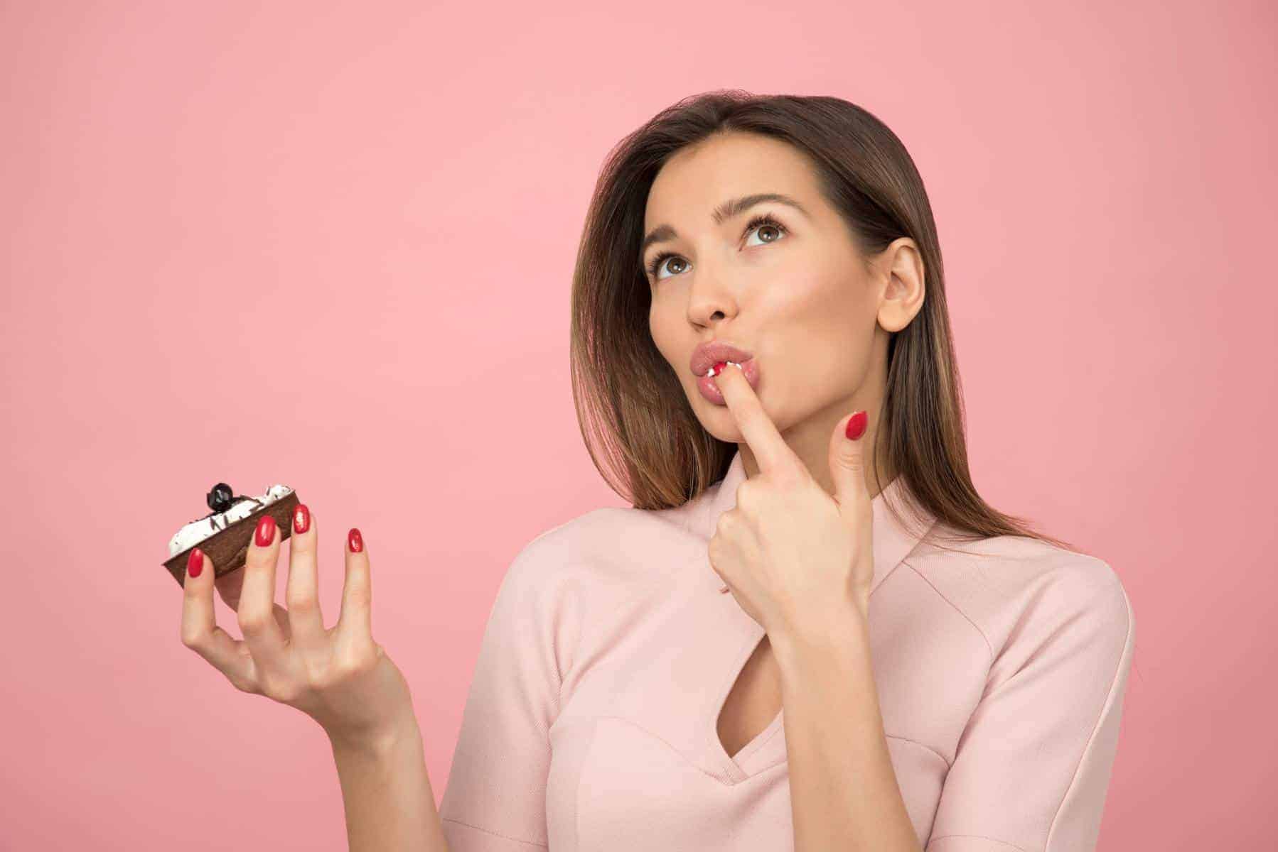 Woman tasting cake frosting with her finger.