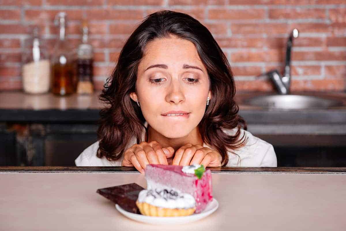 Food Cravings: Woman looking longingly at a piece of cake on the counter.
