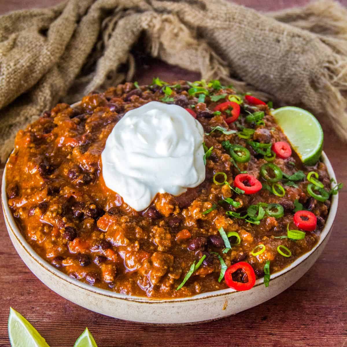 Bowl of Black Bean Chili Topped with Sour Cream, Red and Green Jalapeno Slices, Cilantro, and a Lime Wedge.