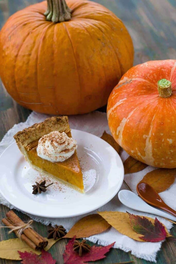 dairy-free keto pumpkin pie with coconut whipped cream and pumpkins on a table
