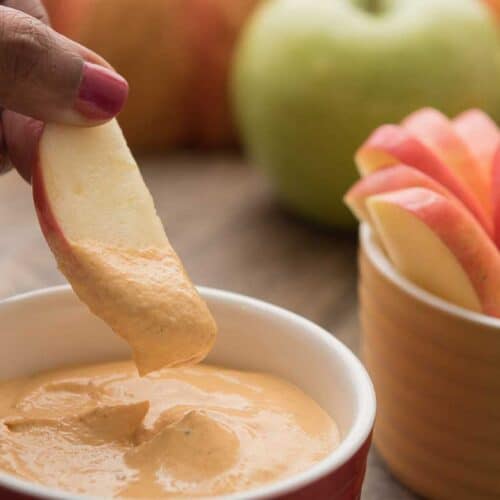 woman dipping an apple slice into pumpkin pie dip