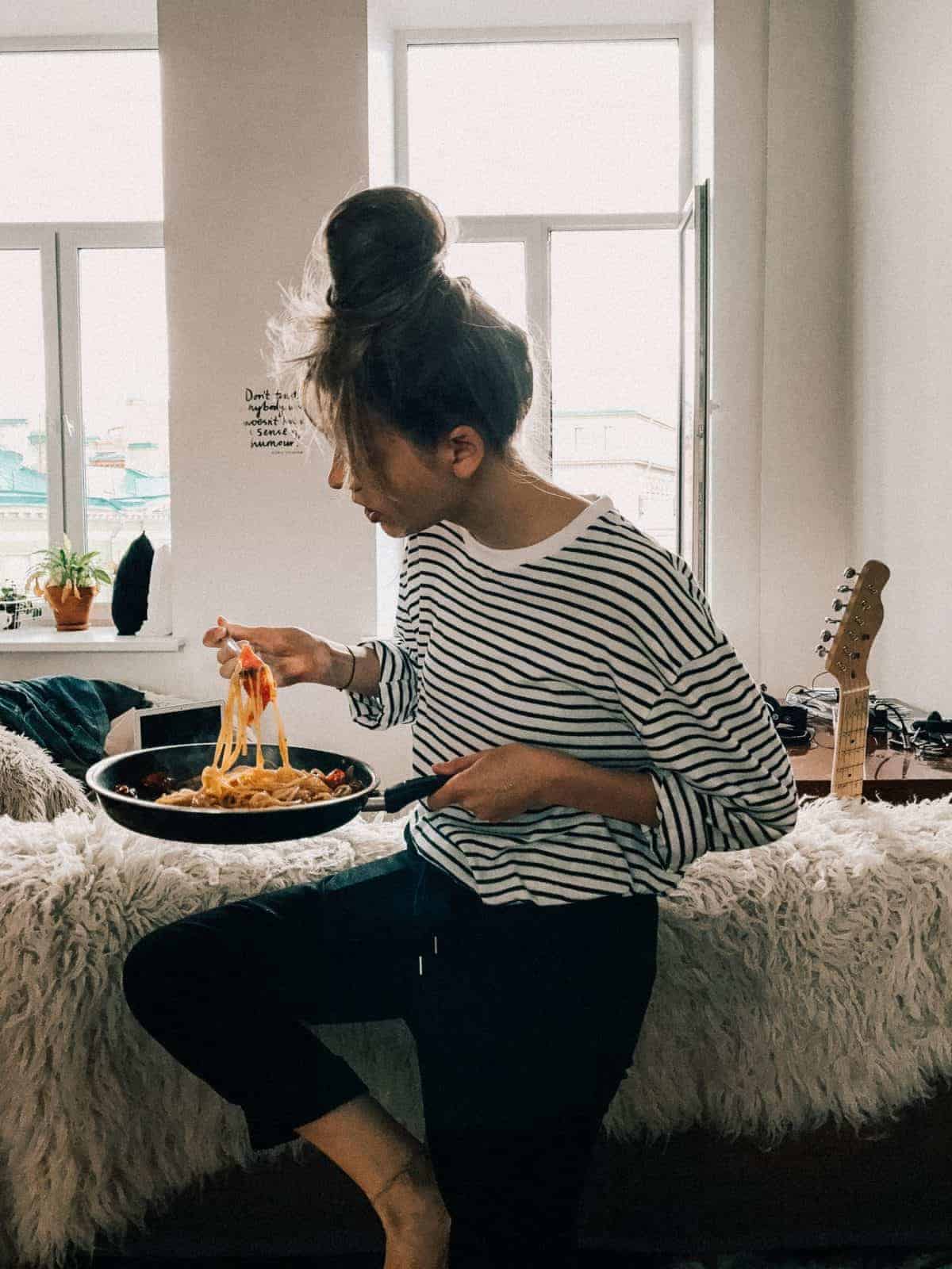 woman eating pasta out of the pan in her bedroom - how to overcome emotional eating