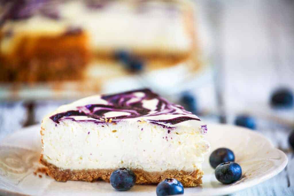 A slice of delicious homemade blueberry marble cheesecake with graham cracker crust and fresh blueberries. Selective focus with extremely shallow depth of field.