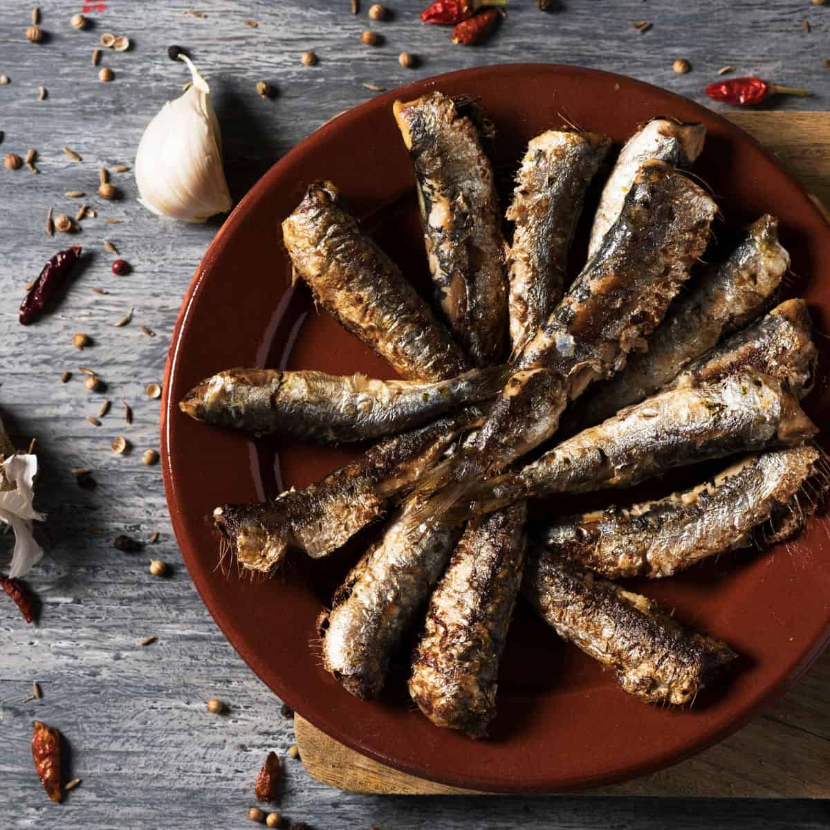 sardines arranged in a star shape on a red plate with dried peppers and garlic