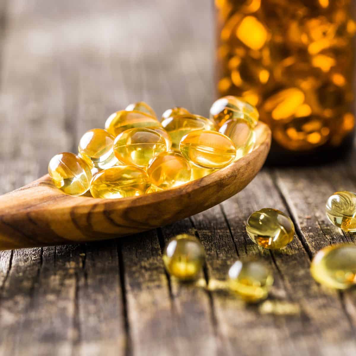 scoop of fish oil gel capsules on a wooden spoon