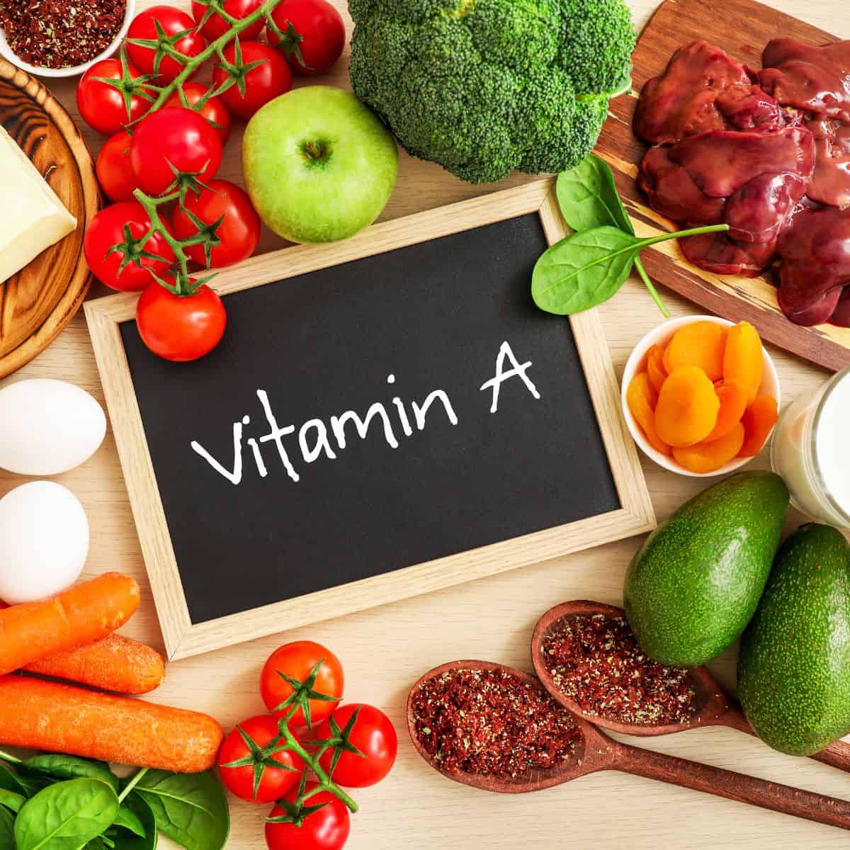 Chalkboard that says vitamin a surrounded by beef liver, tomatoes, broccoli, green apple, eggs, carrots, nuts, and seeds.