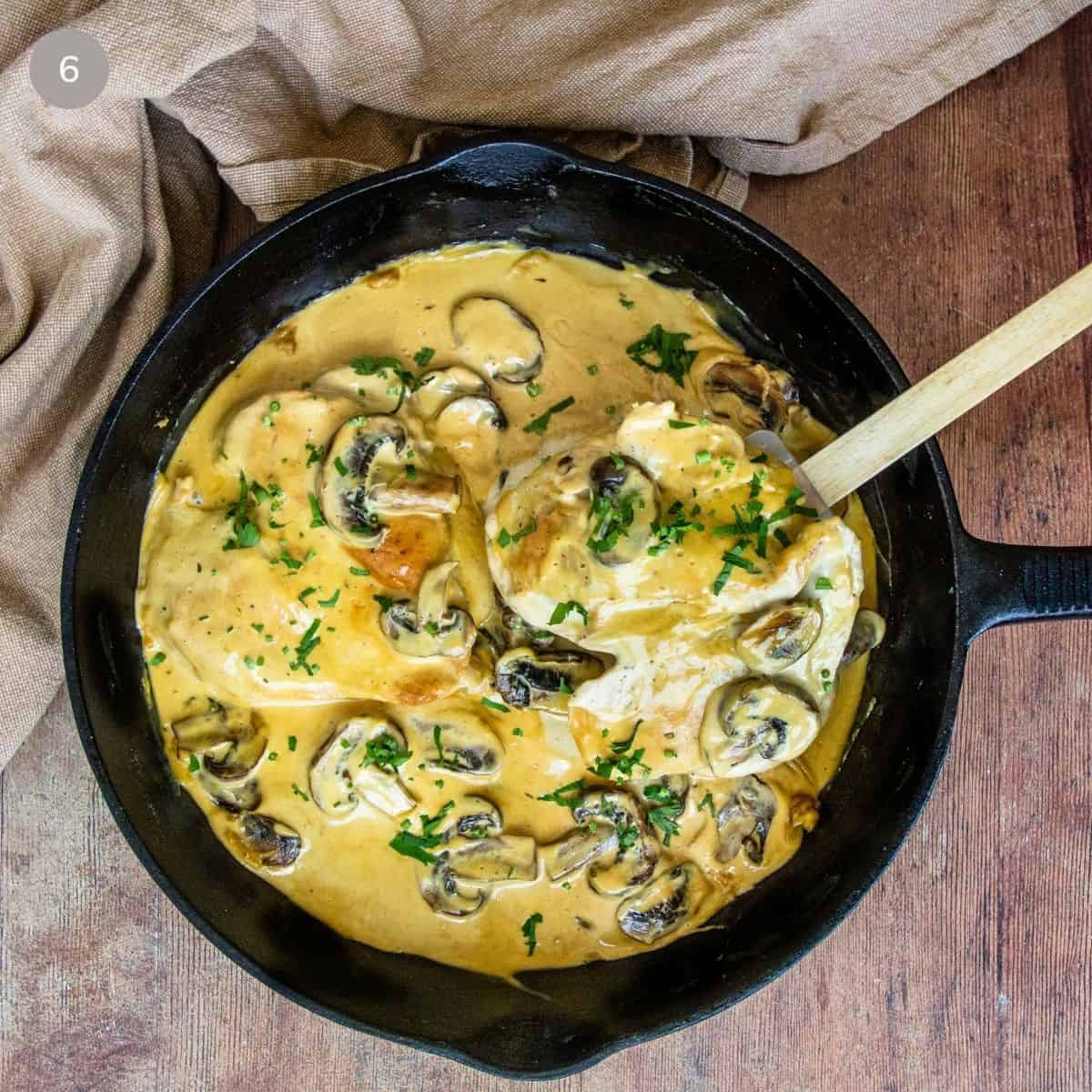 Finished Dijon chicken and mushrooms garnished with parsley in a cast iron skillet with a wooden spoon.